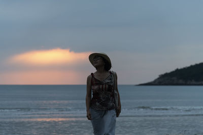 Woman standing at beach against sky during sunset