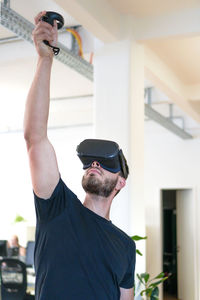 Young man with arms raised using virtual reality simulator at home