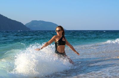 Full length of woman splashing water in sea against sky
