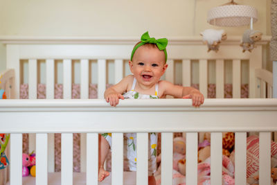 Portrait of happy baby girl standing in crib at home