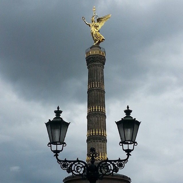 low angle view, sky, lighting equipment, street light, cloud - sky, sculpture, statue, art and craft, art, cloudy, built structure, architecture, cloud, human representation, creativity, animal representation, lamp post, high section, outdoors