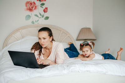 Work from home with kids children. mother working on laptop in bedroom with child daughter toddler 