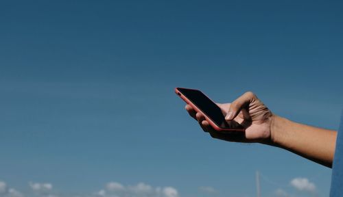 Midsection of person holding mobile phone against blue sky