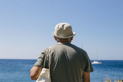 Rear view of man standing by sea against clear sky