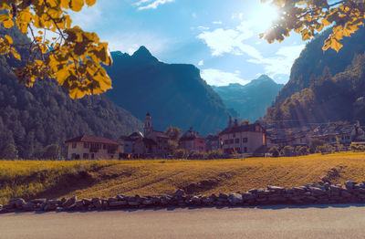 Scenic view of field by houses and mountains against sky