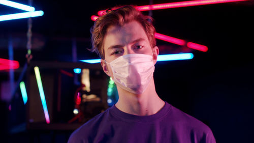 Portrait of young man standing against illuminated wall at night