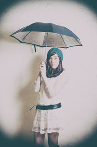 Portrait of mid adult woman holding umbrella while standing against wall