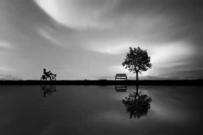 Silhouette tree by swimming pool against lake against sky