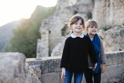 Portrait of siblings standing against stone wall