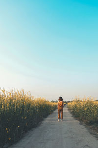 Rear view of woman standing on road amidst plants