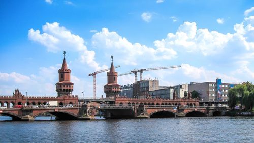 Bridge over river in city against cloudy sky