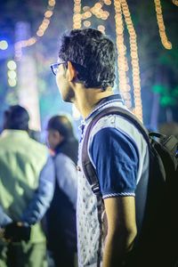 Side view of man standing against illuminated lights at night