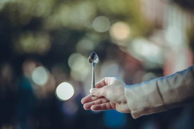 Cropped hand of woman holding heart shape spoon outdoors