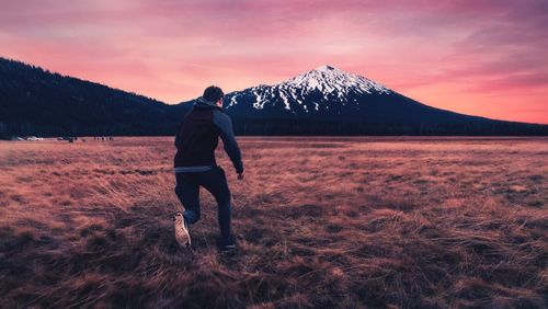 Man standing on snowcapped mountain against sky during sunset