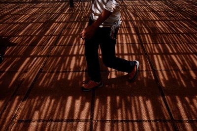 Low section of man walking on boardwalk with on shadow