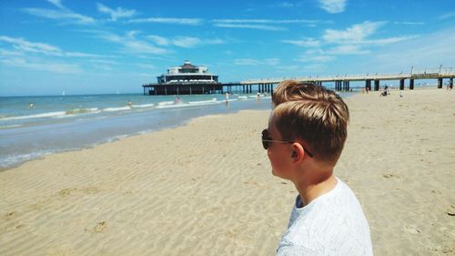 Side view of boy standing at beach against blue sky