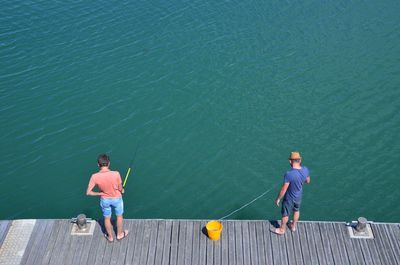 High angle view of men fishing while standing on pier at lake