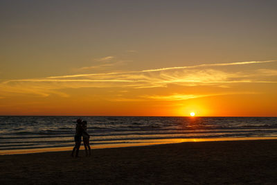 Silhouette people on beach against sky during sunset