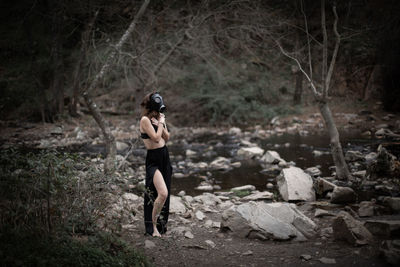 Side view of woman wearing gas mask while covering chest in forest