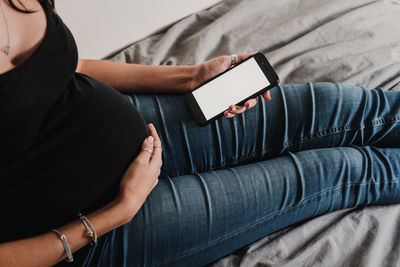 Midsection of woman using phone while sitting on bed at home