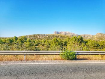 Road by trees against clear blue sky