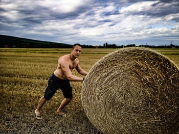 Full length of man with hay bales on field against sky