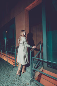 Woman standing by railing against building at night