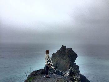 Rear view of person standing on rock by sea