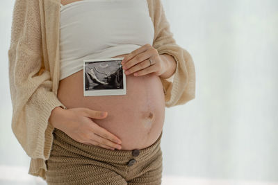 Midsection of woman holding book while standing against wall