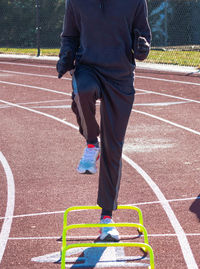 Front view ofr a runner in the a-position standing over yellow mini banana hurdles on a track.