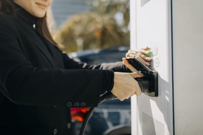 Young woman plugging electric charger at charging point