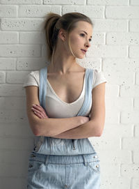 Thoughtful young woman looking away while standing against wall