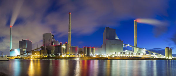 Large illuminated coal power plant with reflected lights in the water of a river