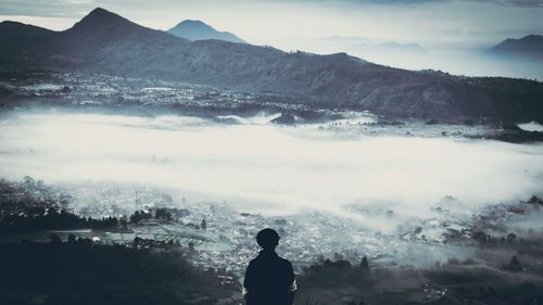 Rear view of boy against mountain during foggy weather