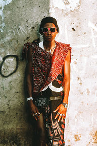 Portrait of young man wearing sunglasses standing against wall