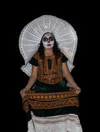 Portrait of young woman standing against black background