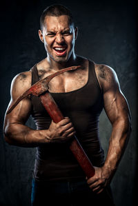 Aggressive muscular man holding pick axe against wall