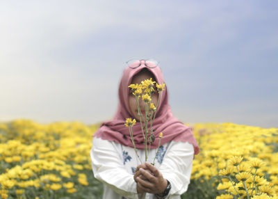 Midsection of person holding yellow flower in field