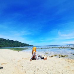 Full length of man sitting on beach against blue sky