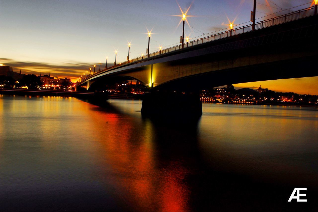 ILLUMINATED SUSPENSION BRIDGE OVER RIVER AT NIGHT