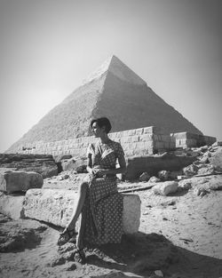 Full length of young woman sitting against pyramid