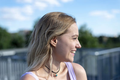 Close-up of thoughtful smiling young woman with blond hair against sky