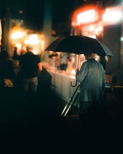 Rear view of man walking on wet street at night