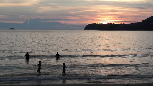 Silhouette people on beach against sky during sunset