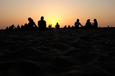Silhouette people on beach against clear sky during sunset