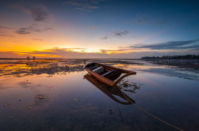 Abandoned boat on shore against sky during sunset