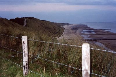 Wooden fence in grass against sky