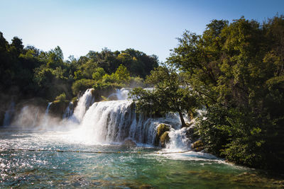 Scenic view of waterfall in forest against sky