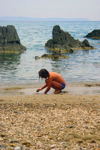 Rear view of man on rock at beach against sky