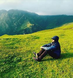 Side view of man sitting on landscape against mountain